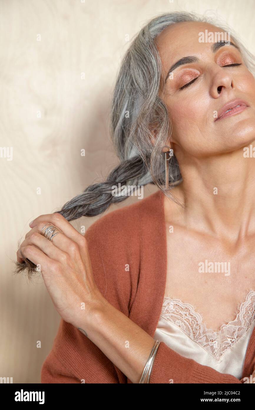 Primo piano ritratto di una donna di mezza età con capelli grigi, guardando fuori dalla fotocamera con gli occhi chiusi Foto Stock