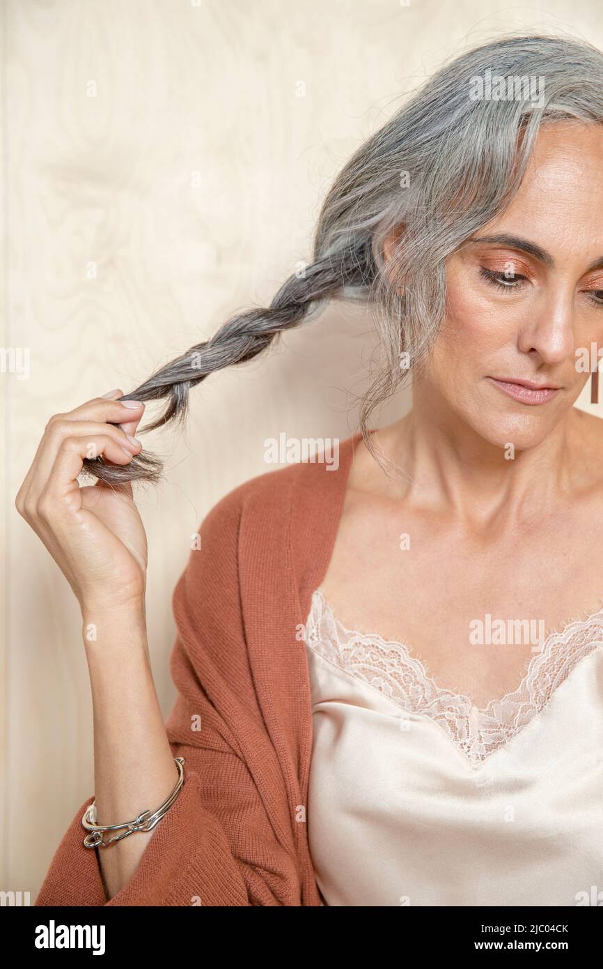 Giovane donna con capelli grigi guarda giù fuori macchina fotografica tenendo la sua coda di pony. Foto Stock