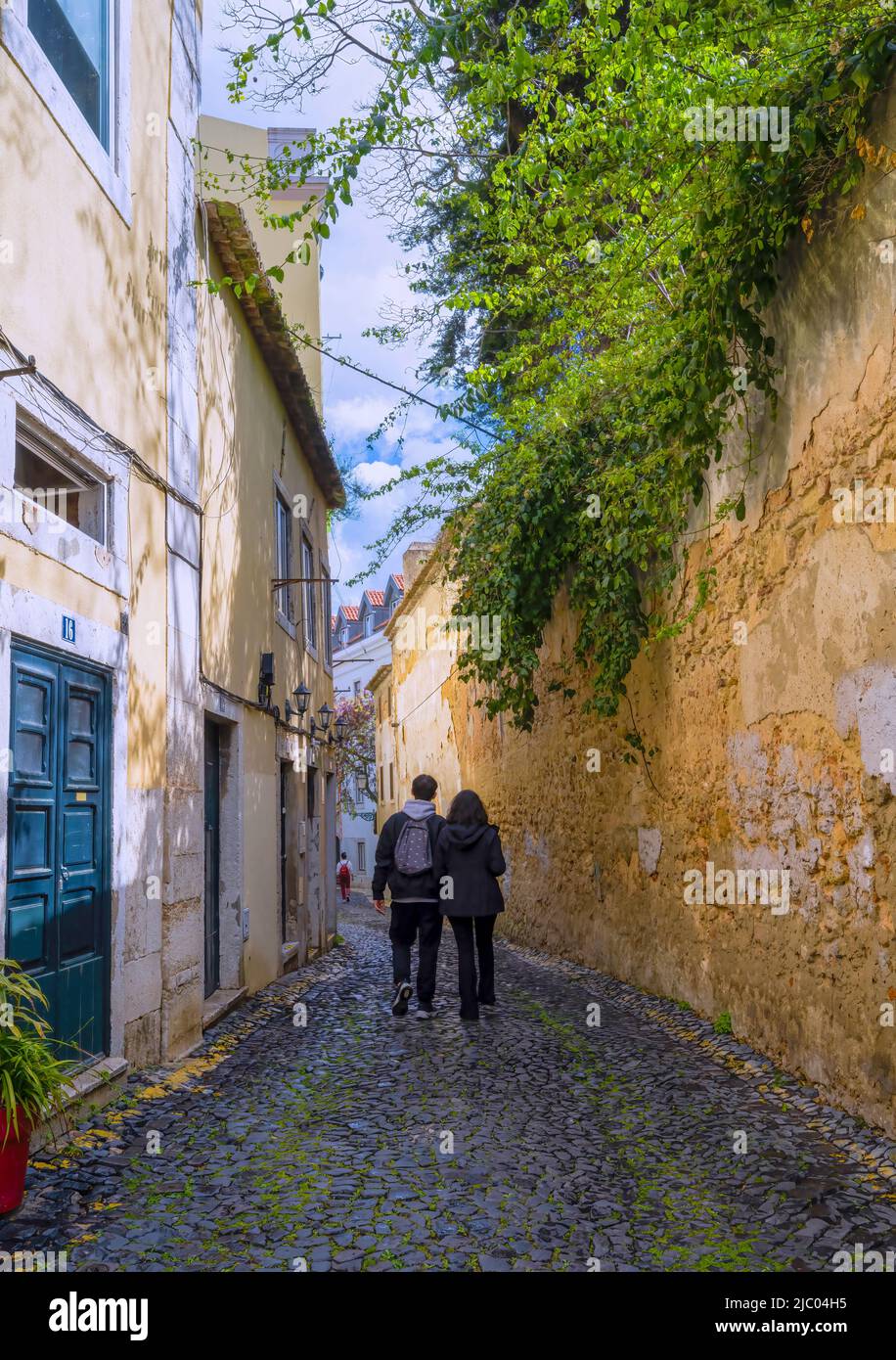 Un giovane uomo e una donna camminano lungo una stradina acciottolata nel centro di Lisbona, capitale del Portogallo Foto Stock