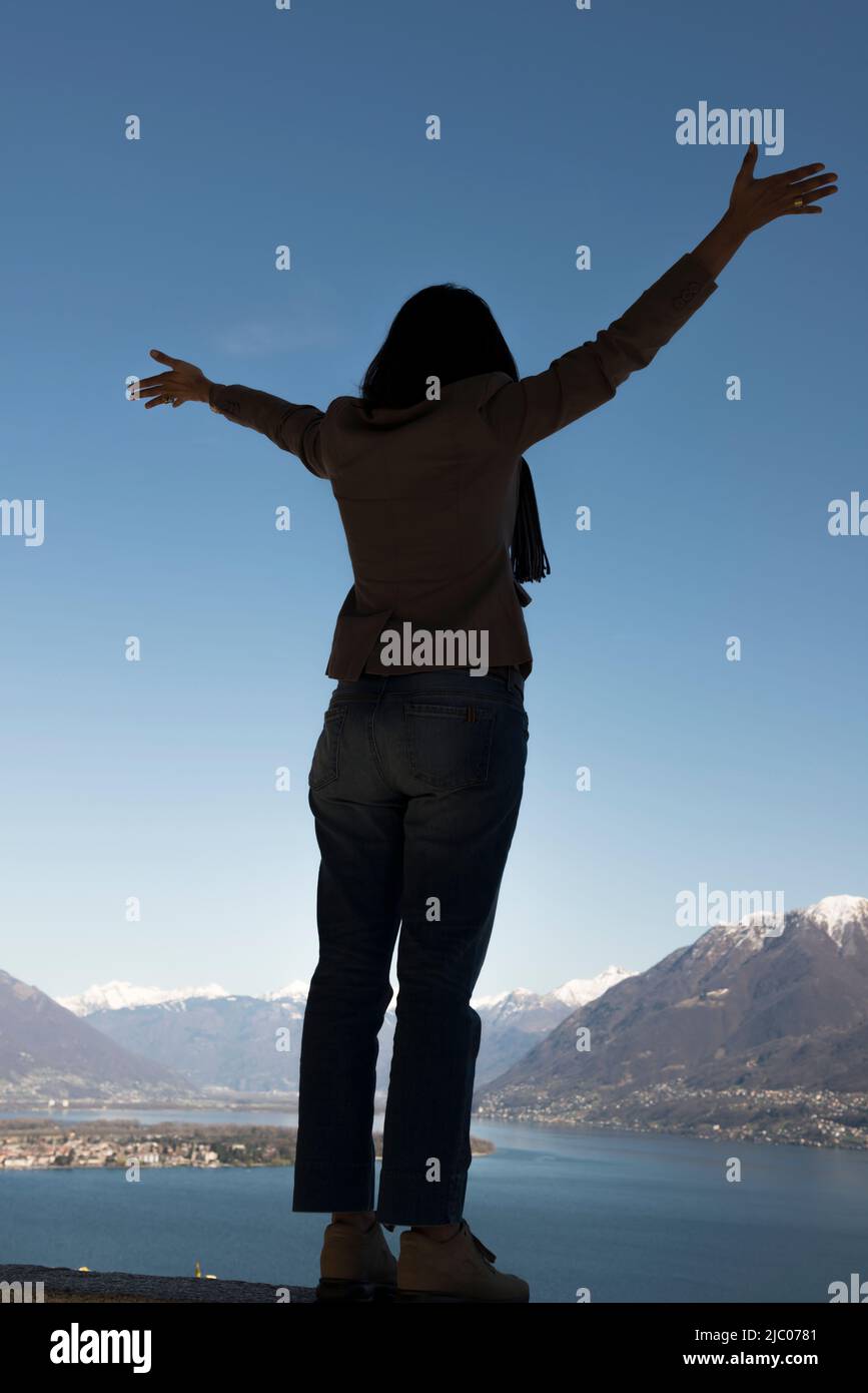 Donna con le braccia distese e godere della vista panoramica sul Lago Alpino maggiore con la montagna innevata ad Ascona, Svizzera. Foto Stock