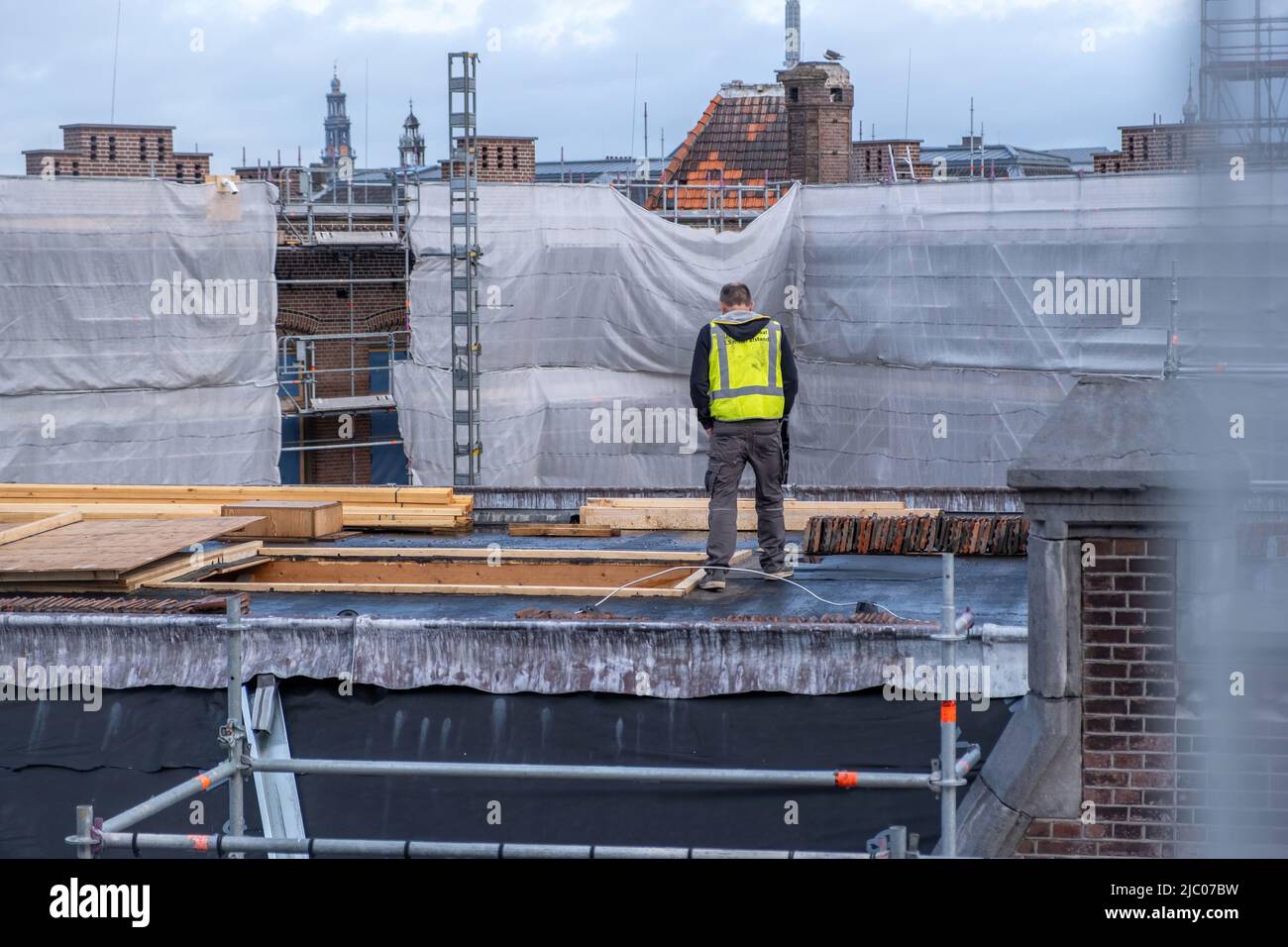 Costruzione di tetti lavori di isolamento. Lavoratore con gilet giallo sul tetto, impalcatura in metallo. Amsterdam, Paesi Bassi Foto Stock
