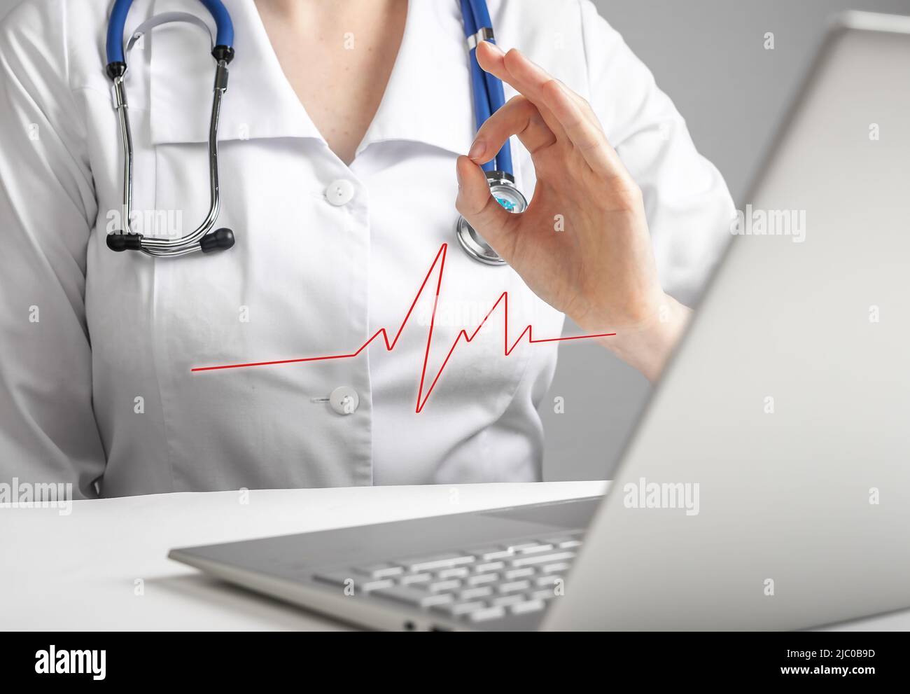 Il medico segnala i risultati dell'elettrocardiogramma al paziente online utilizzando un computer portatile. Telemedicina, concetto di telesaluità. Donna in camice da laboratorio che non mostra problemi di cuore con il gesto della mano ok tramite videocall. Foto Foto Stock