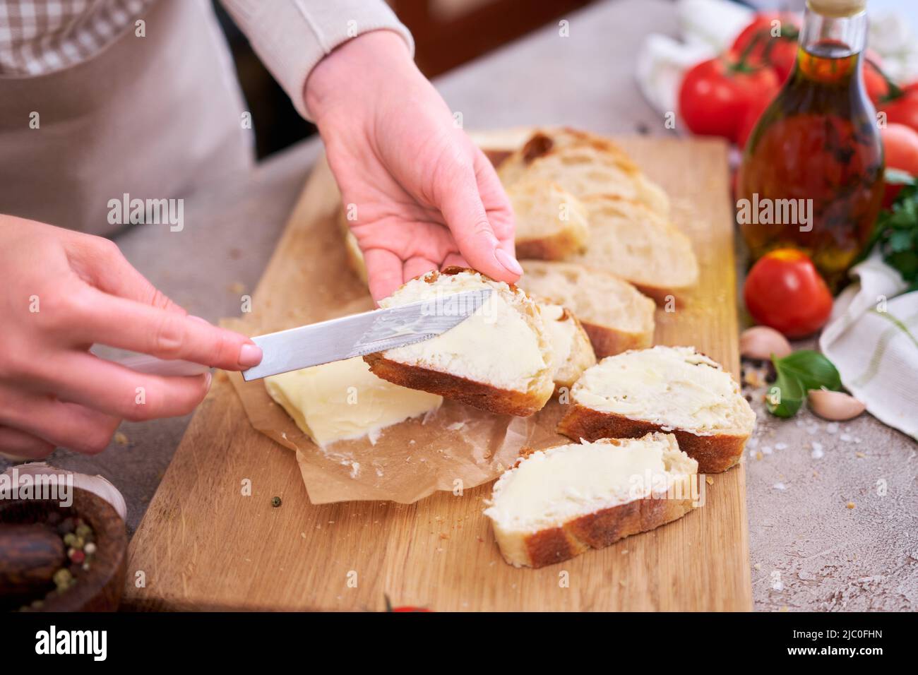 Donna che spalma il gustoso burro organico sul pane sopra la tavola grigia con tagliere in legno Foto Stock
