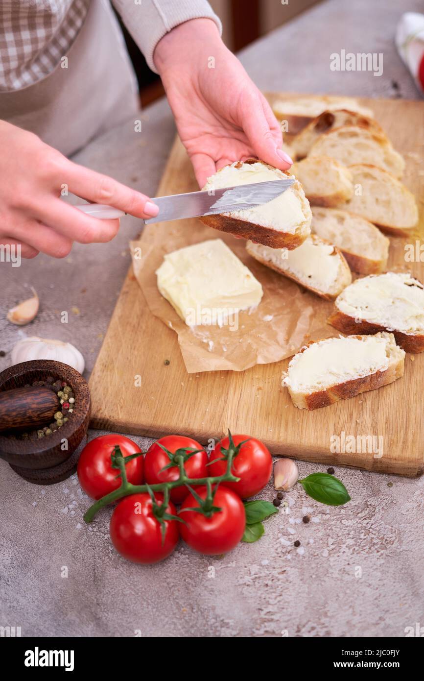 Donna che spalma il gustoso burro organico sul pane sopra la tavola grigia con tagliere in legno Foto Stock