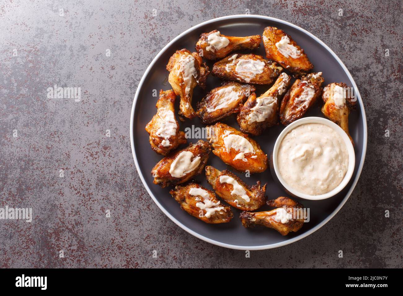 Porzione di ali di pollo alla griglia con salsa barbecue bianca Alabama da vicino in un piatto sul tavolo. Vista dall'alto orizzontale Foto Stock