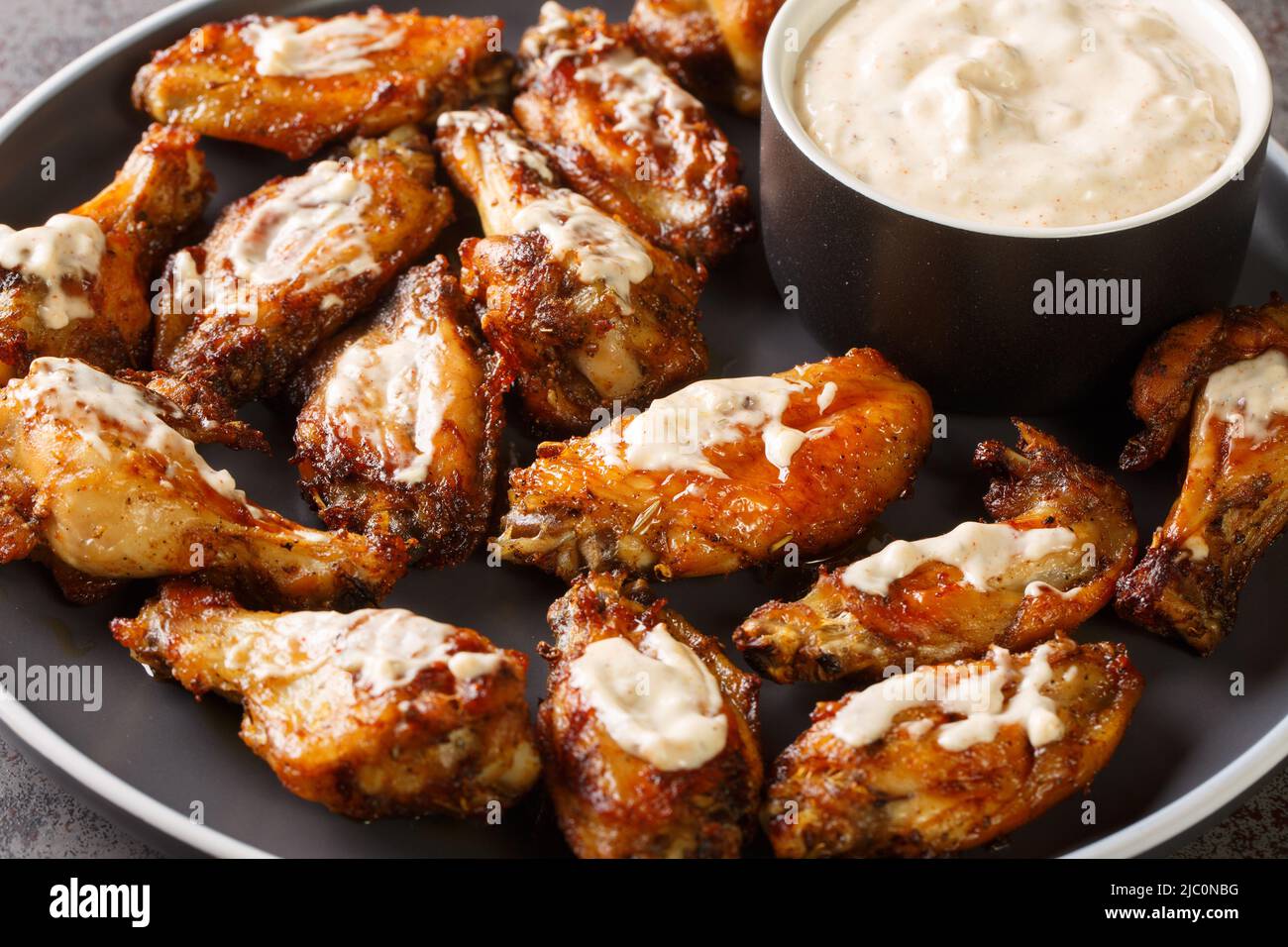 Gustose ali di pollo con salsa barbecue bianca Alabama da vicino in un piatto sul tavolo. Orizzontale Foto Stock