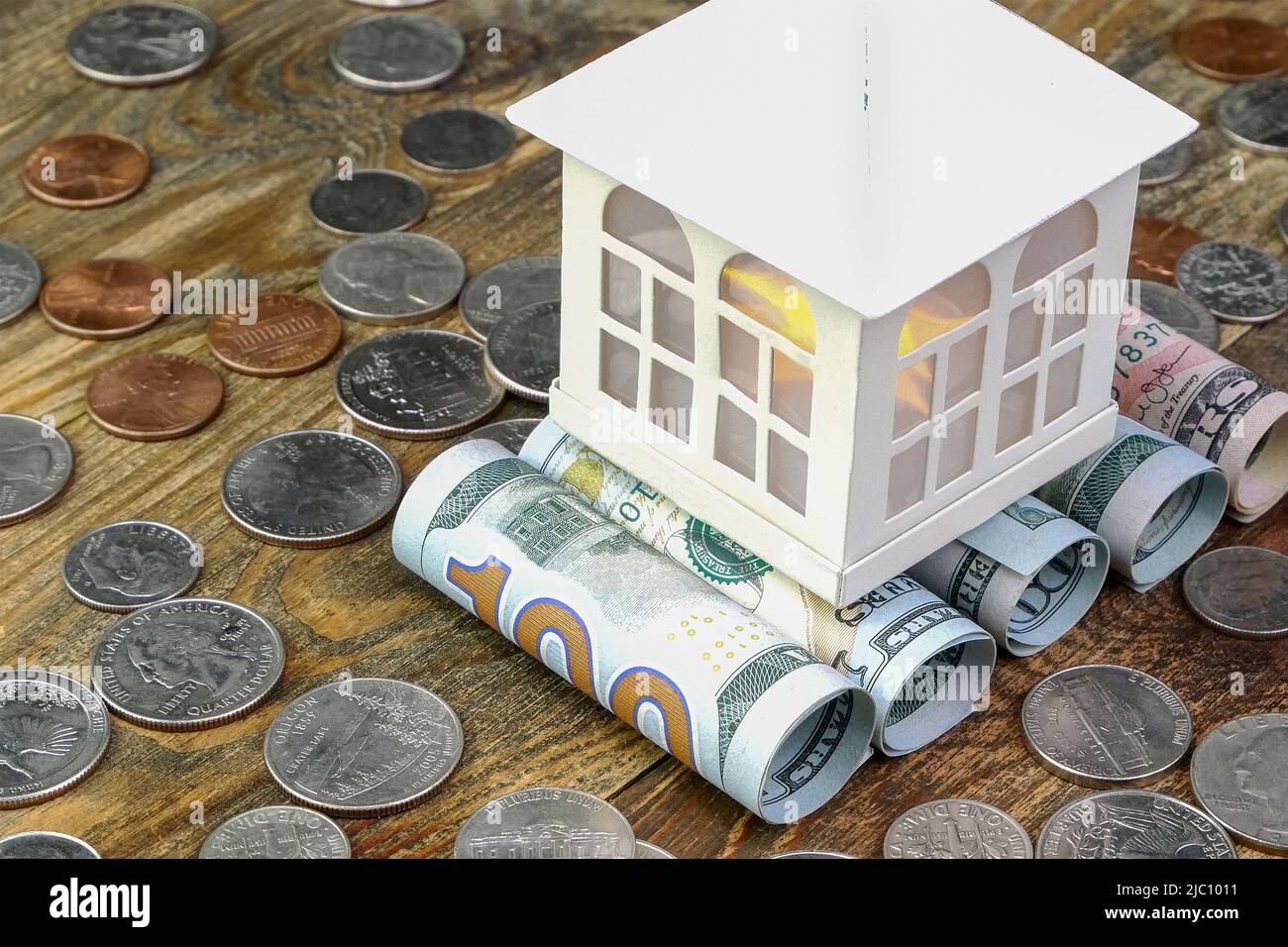 Casa in cima alle banconote in dollari americani arrotolati in tubo e molti noi monete. Cassa domestica e risparmio di beni finanziari per investimenti immobiliari Foto Stock