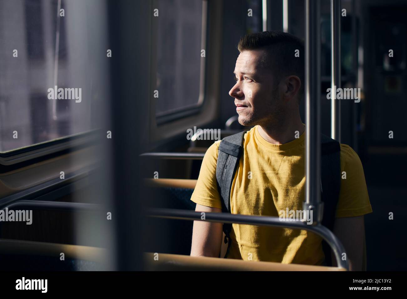 Uomo solitario pensivo che guarda fuori dalla finestra del treno. Solo in trasporto pubblico in giorno di sole. Foto Stock