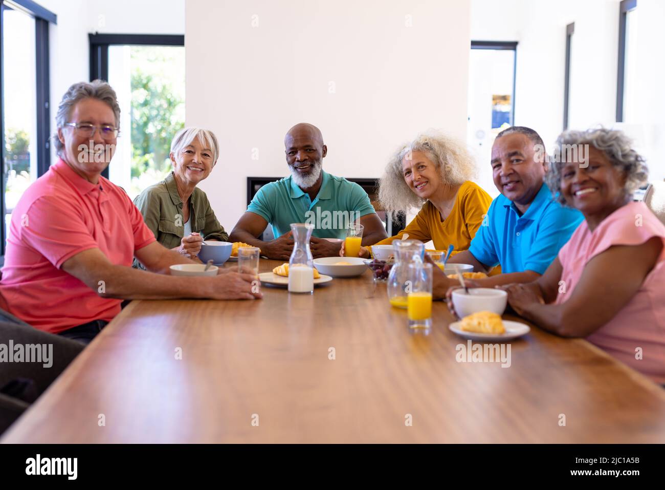 Ritratto di amici anziani multirazziale felice con cibo e bevande sul tavolo da pranzo in casa di cura Foto Stock