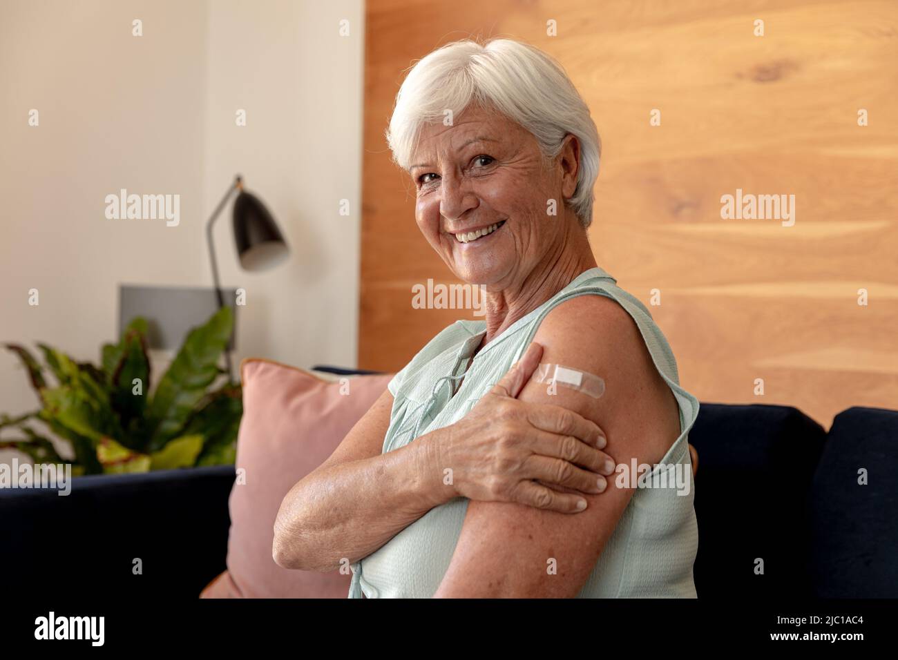 Ritratto della donna anziana caucasica sorridente mentre tiene il braccio con l'aiuto della fascia seduta sul divano Foto Stock