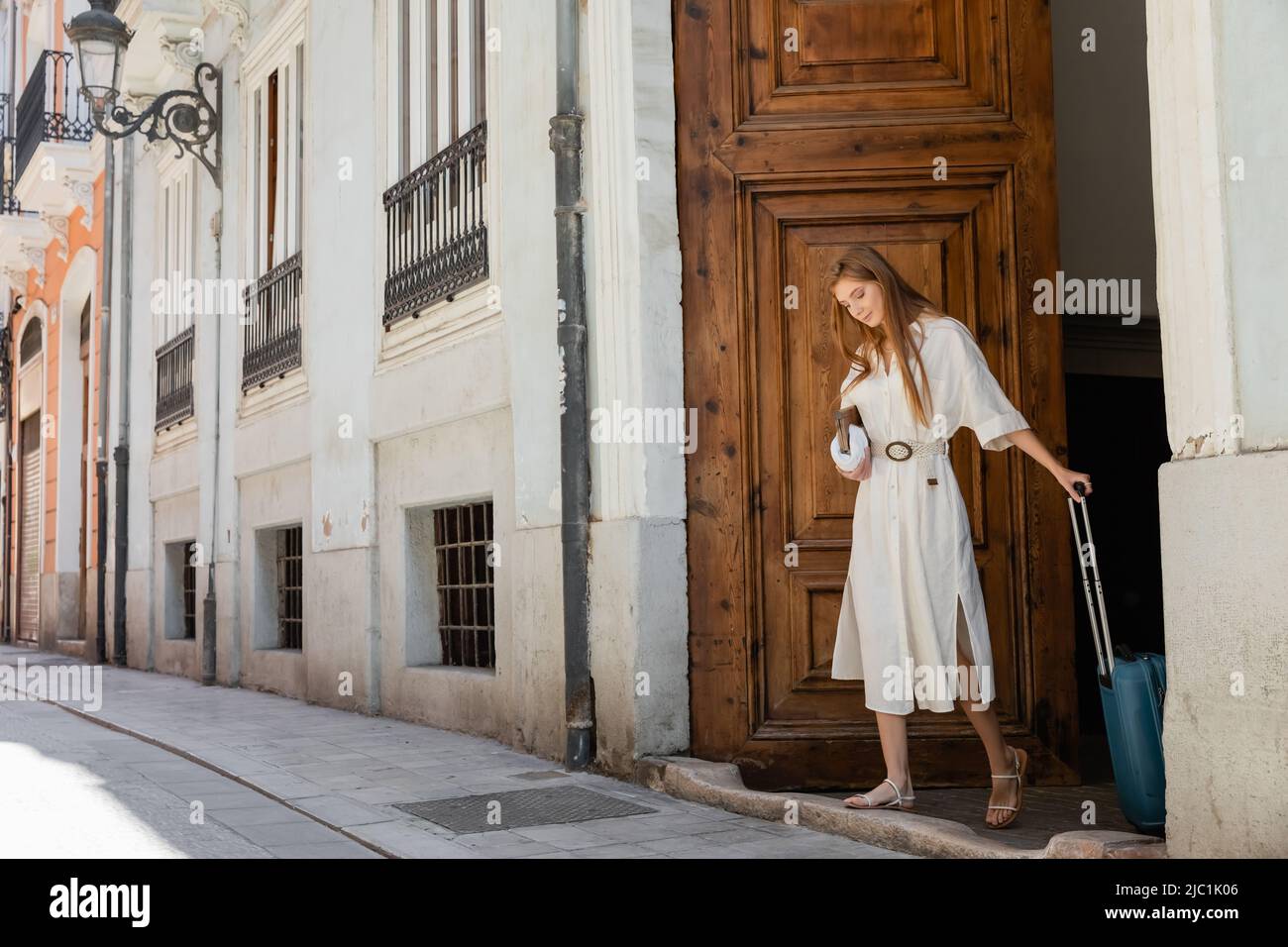 donna rossa che tiene la borsa e la valigia vicino alla porta di ingresso in legno a valencia Foto Stock