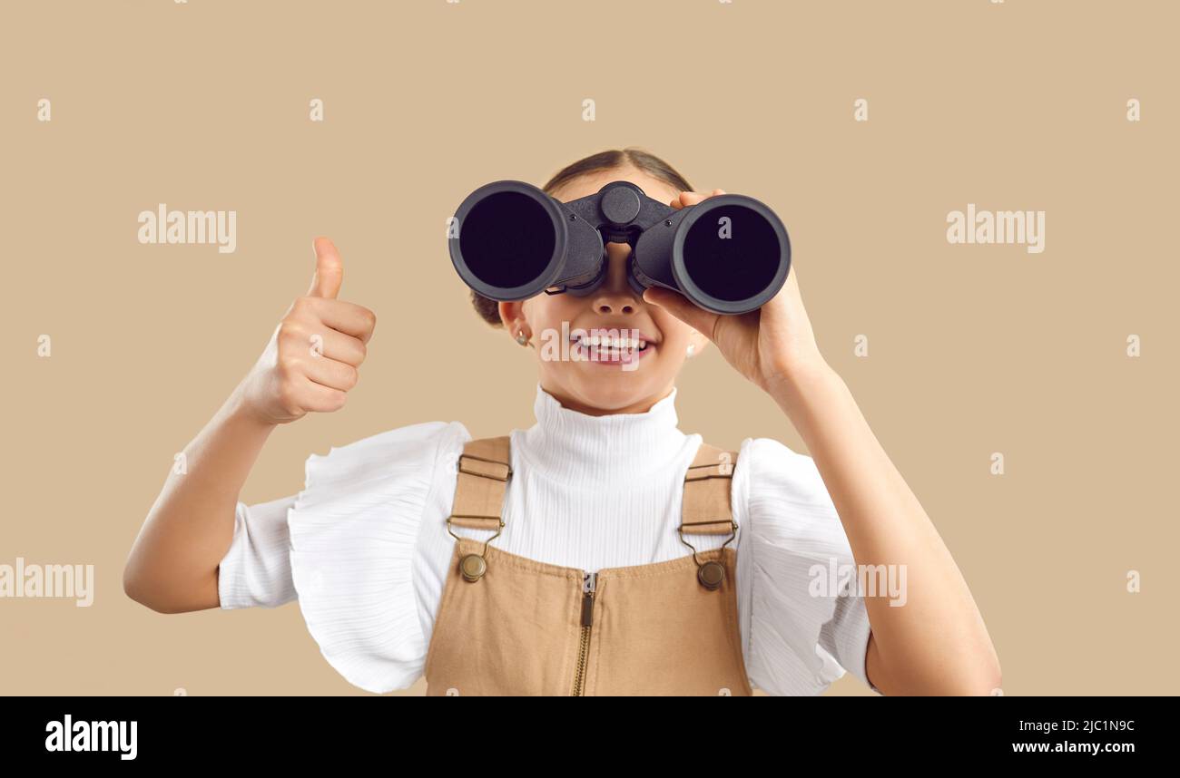 Happy Kid explorer guardando attraverso binocoli, facendo scoperte e mostrando pollici in su Foto Stock