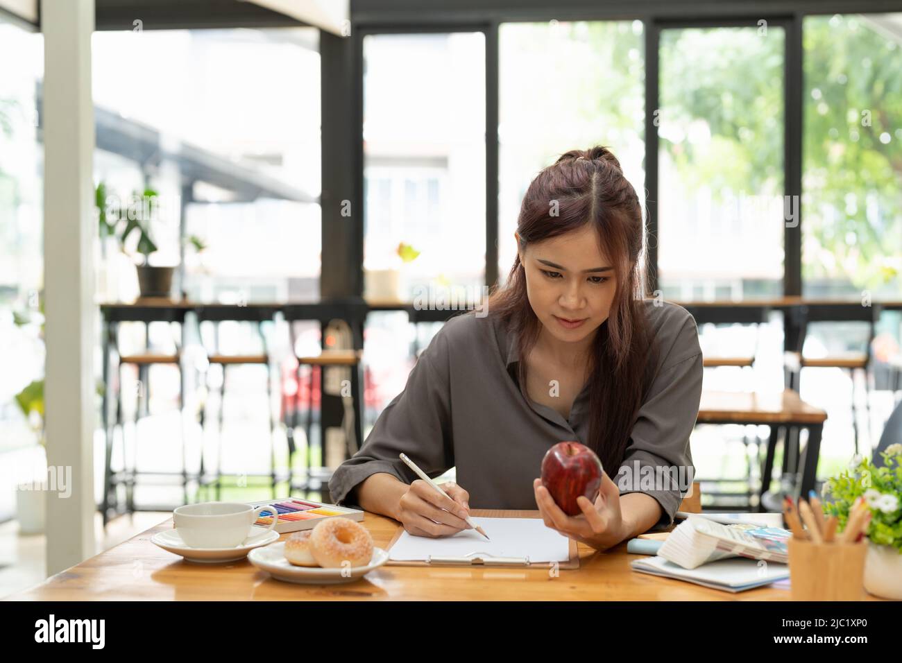 Giovane grafica femminile asiatica che disegna mela sul suo progetto con un moderno luogo di lavoro creativo Foto Stock