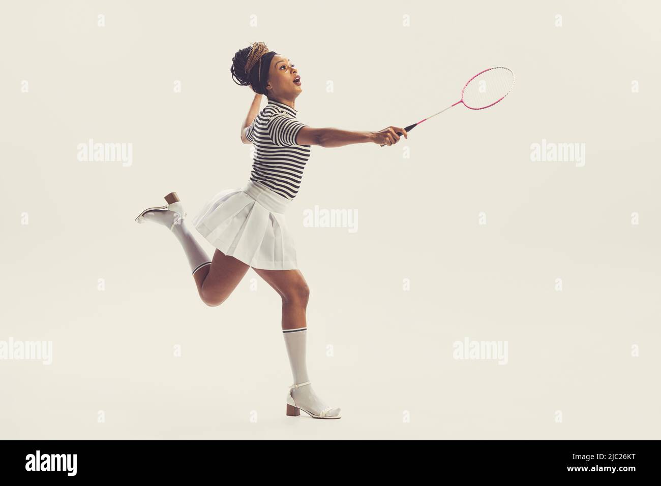 Ritratto di giovane felice bella donna in retrò, 70s, 80s abiti moda stile, vestito vintage giocando badminton isolato su sfondo bianco Foto Stock