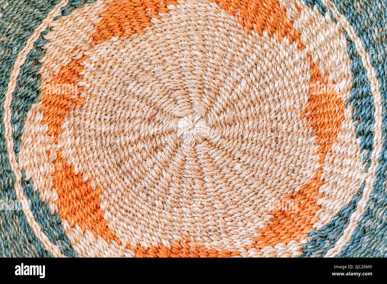 Fibre di iuta arrotolate formano un motivo circolare a tappeto in crema, arancione e blu-verde spento, creando uno sfondo tessile intrecciato dettagliato. Foto Stock
