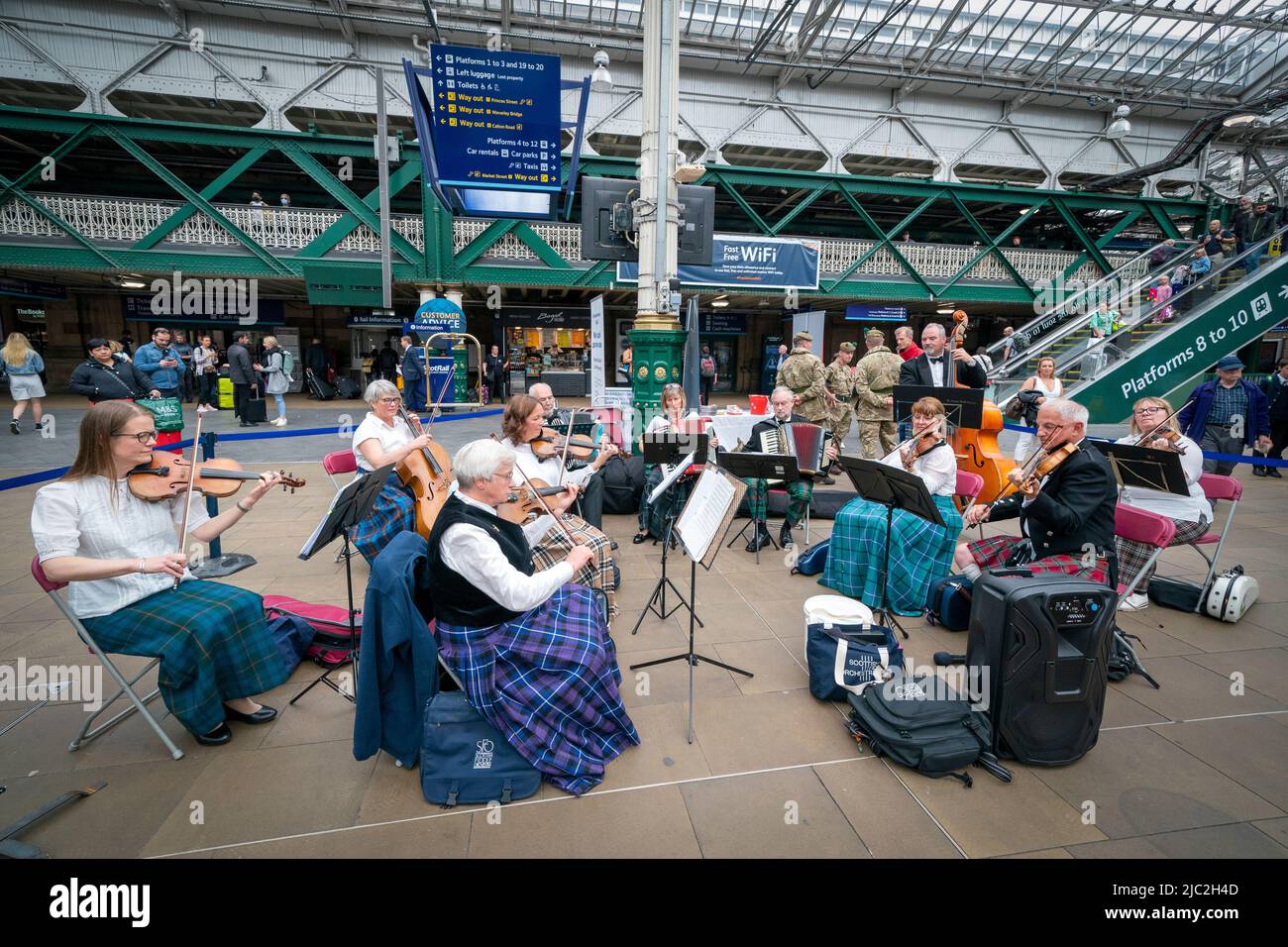 I membri della Scottish Fiddle Orchestra suonano in un pop-up presso la stazione Waverley di Edimburgo, in un breve concerto di brani tradizionali del loro repertorio per intrattenere i passanti nella corte davanti al loro prossimo concerto presso Usher Hall il sabato. Data foto: Giovedì 9 giugno 2022. Foto Stock