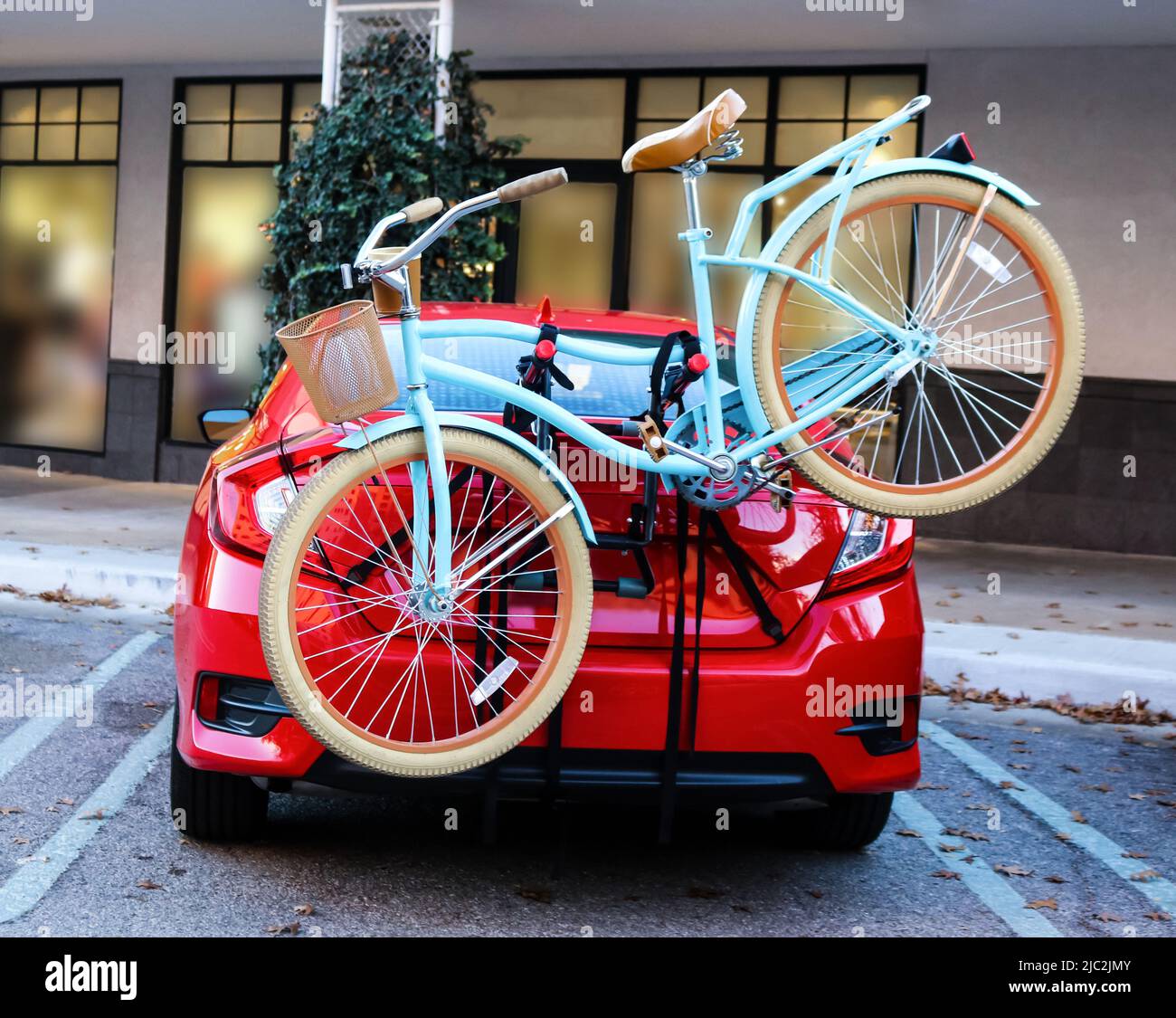 Biciclette blu con cesto fissato al retro del rosso sport auto parcheggiate davanti ai negozi Foto Stock