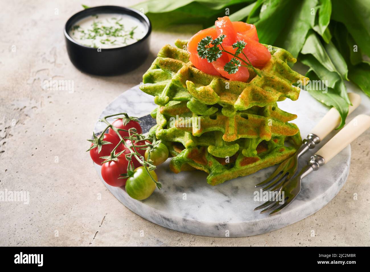 Waffle belgi verdi. Spinaci o aglio selvatico o pesto cialde con salmone rosso e salsa di panna su sfondo grigio tavolo di cemento. Deliziosa colazione, Foto Stock