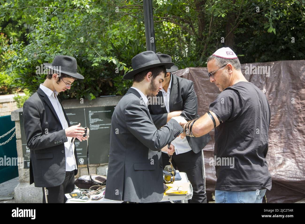 Gli uomini ebrei ortodossi di Hasidic aiutano un altro uomo ebreo a pregare con tefillin al mattino in Union Square Park a New York City. Foto Stock