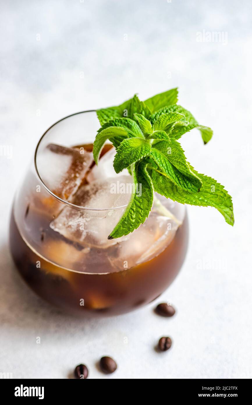 Primo piano di una bevanda a base di caffè ghiacciato su un tavolo con foglie di menta fresca e chicchi di caffè torrefatti Foto Stock