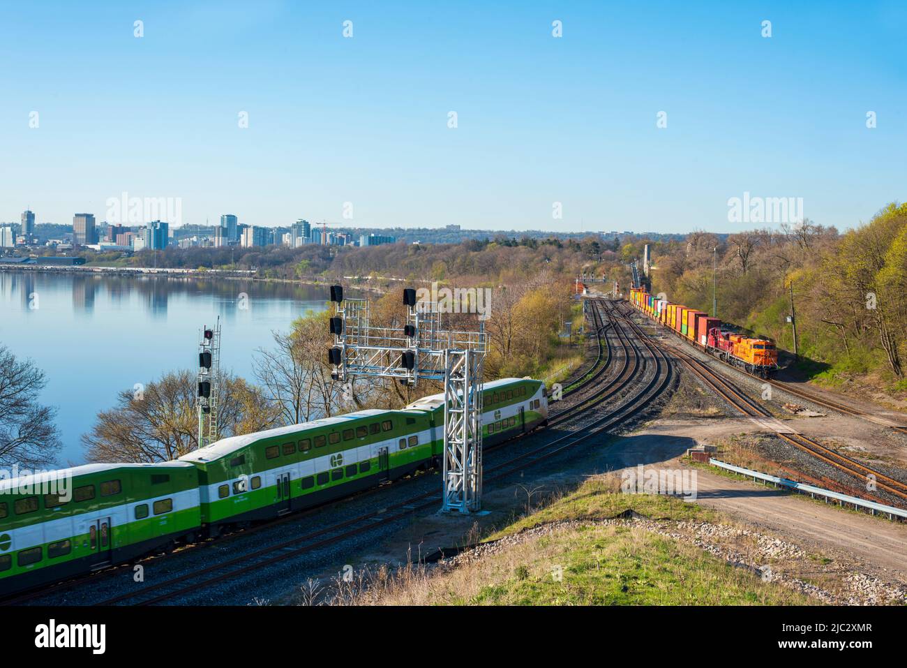 Una foto paesaggistica di UN treno GO Transit e di un treno merci che si affaccia sul porto di Hamilton sul sistema di transito ferroviario Metrolinx. Foto Stock