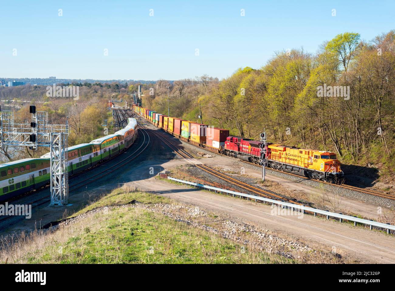 Una foto paesaggistica di UN treno GO Transit e di un treno merci che si affaccia sul porto di Hamilton sul sistema di transito ferroviario Metrolinx. Foto Stock