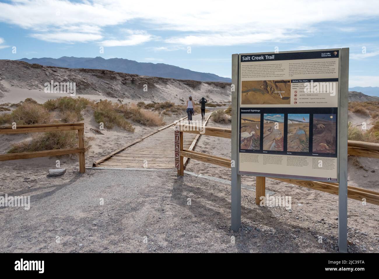 Due bambini si dirigono a piedi dal sentiero interpretativo di Salt Creek, superando il cartello informativo sui pesci cucci e sull'habitat salato del deserto della Death Valley. Foto Stock