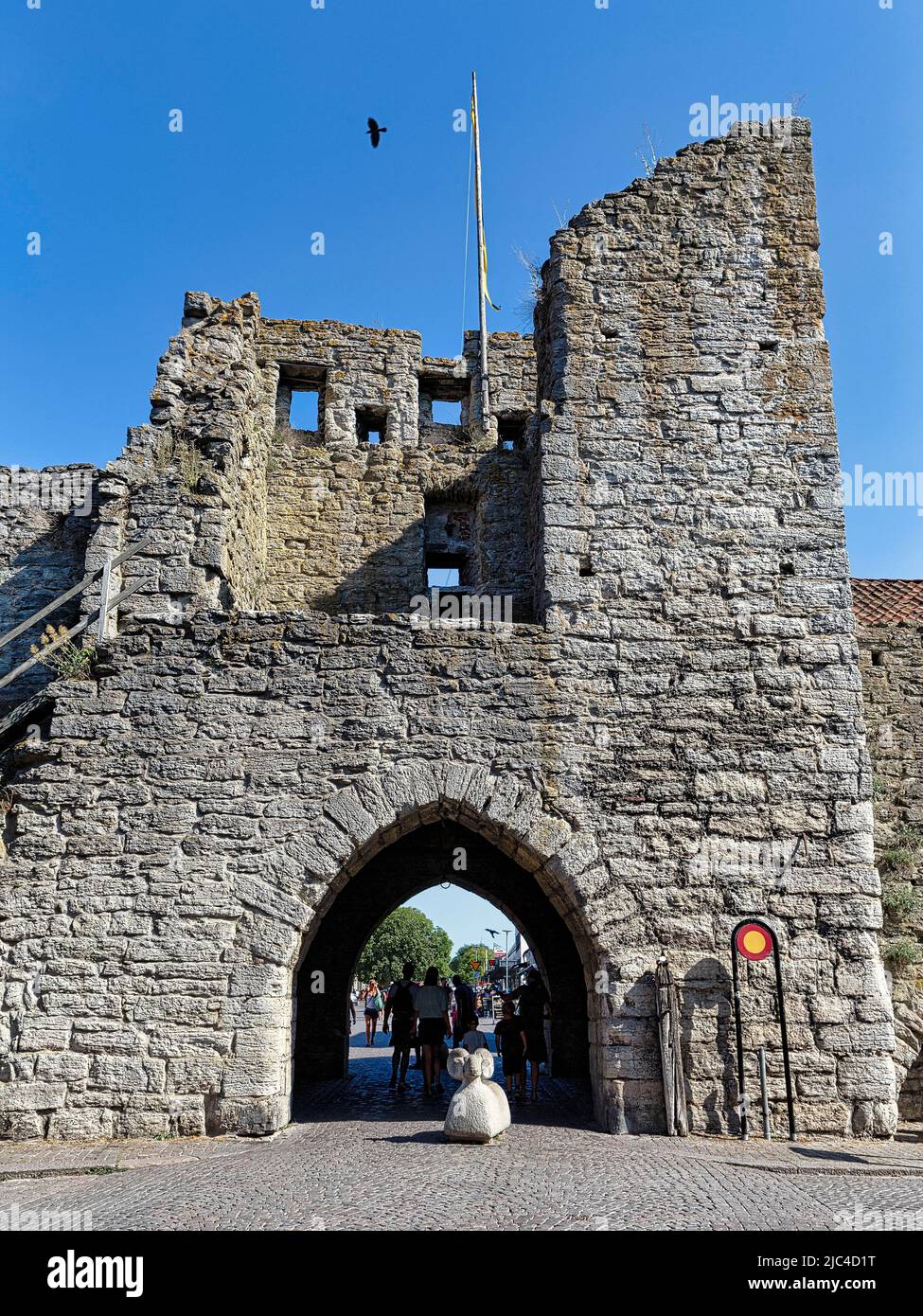 Porta nel muro della città, fortificazione della città con scultura in pietra, pecore Gotland come barriera, bollards nella zona pedonale, città vecchia di Visby, Gotland Foto Stock
