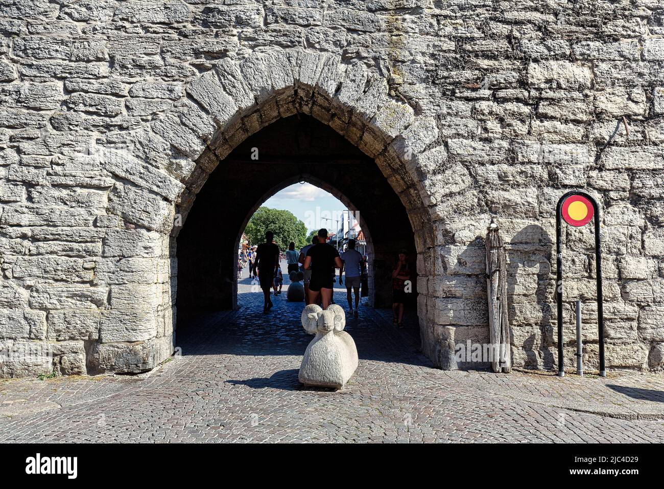 Porta nel muro della città con scultura in pietra, pecore Gotland come barriera, bollards nella zona pedonale, Città Vecchia di Visby, Gotland Island, Svezia Foto Stock