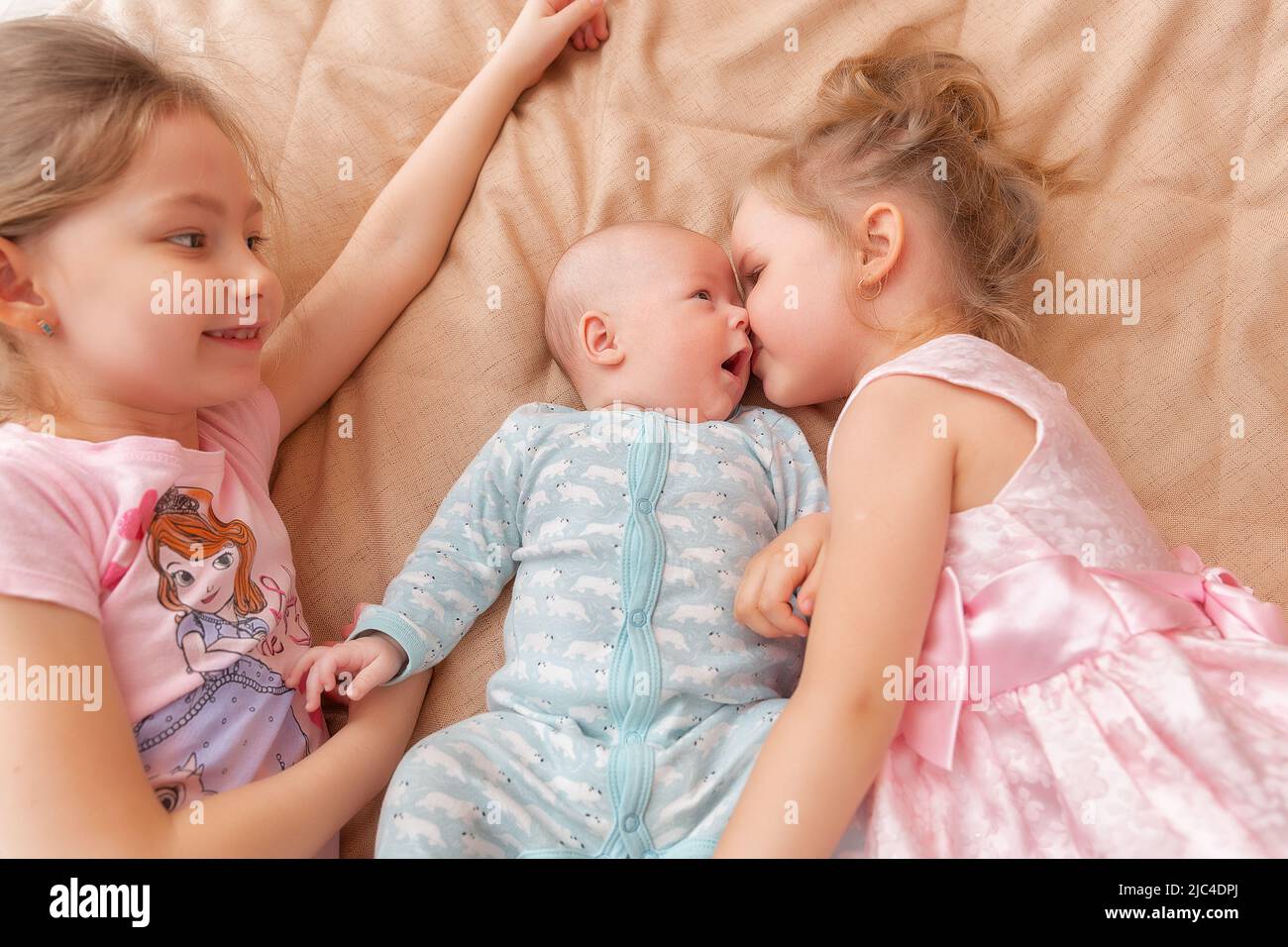 Ritratto di un bambino carino di 3 mesi-vecchio e due ragazze piccole sorelle felici abbracciano su un Male. Bambino neonato che si rilassa in camera da letto. La mattina della famiglia a casa Foto Stock