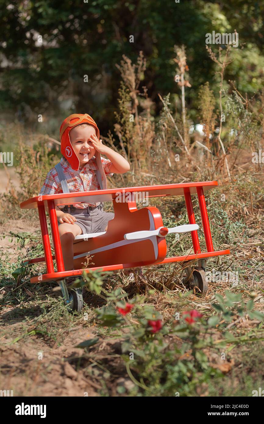Felice ragazzo pilota seduto e giocare con giocattolo aereo rosso in estate. Sogni figlio di viaggio Foto Stock