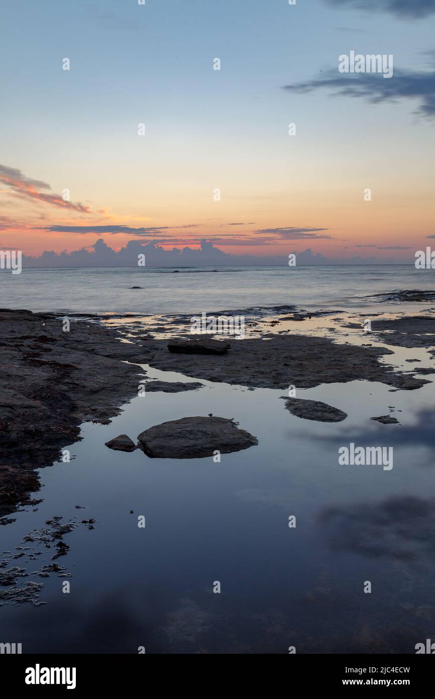 Massi e rocce nel surf sulla costa del Mar Baltico al tramonto, lunga esposizione Foto Stock