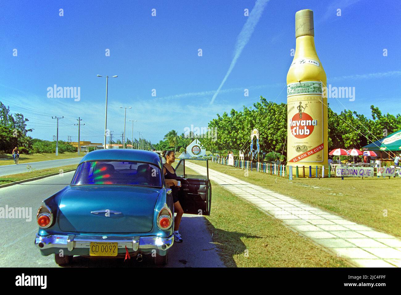 La ragazza cubana esce da un'auto d'epoca, bottiglia di rum Havana Club grande plastica, rum pubblicità a una Fiesta, Santa Lucia, Cuba, Caraibi Foto Stock