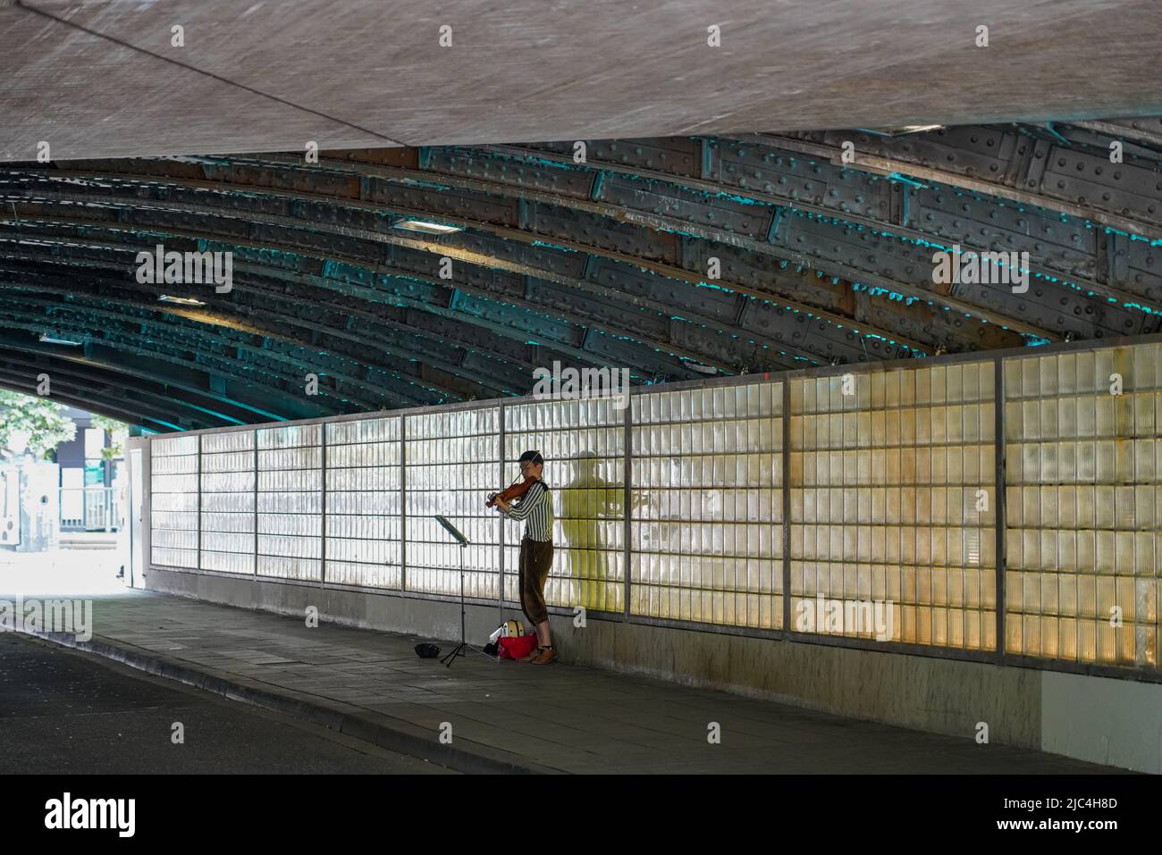 Un musicista di strada asiatico si trova in un tunnel di strada illuminato blu a Colonia e suona il violino, Renania settentrionale-Vestfalia, Colonia, Germania 21.5.22 Foto Stock