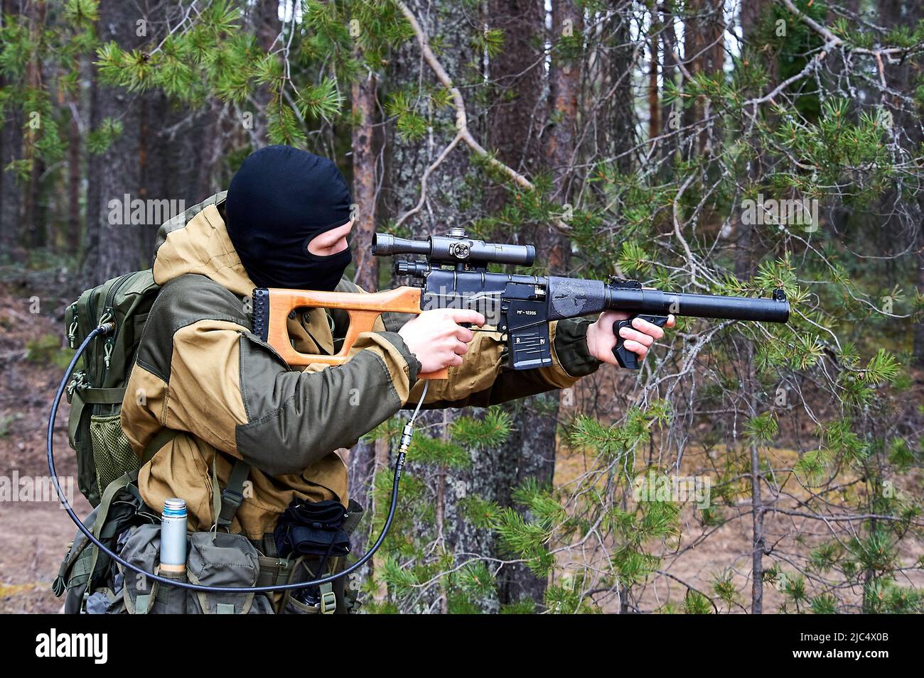 Un uomo in balaclava con un fucile da cecchino che mira nei boschi Foto Stock