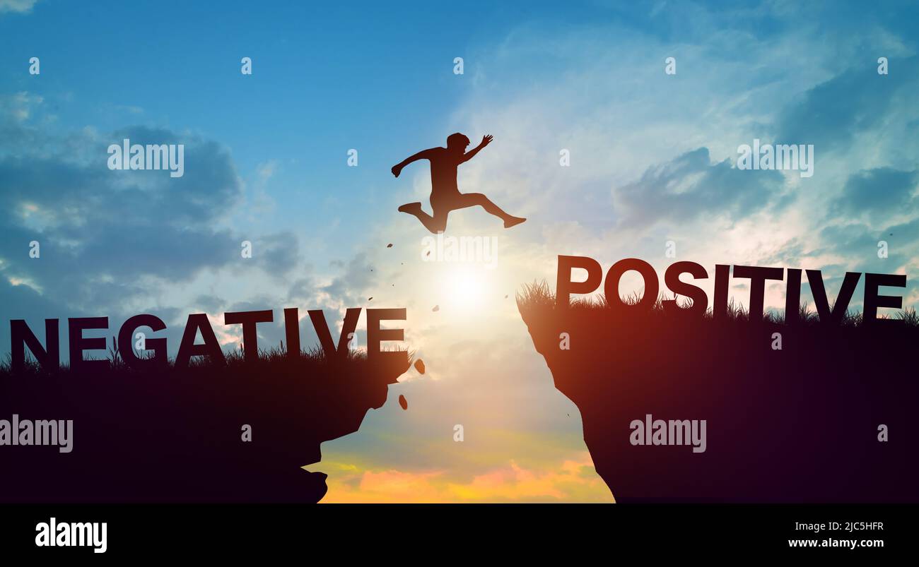 Silhouette uomo che salta su parole negative e positive sulle scogliere con cielo nuvoloso e alba. Mentalità positiva e pensiero positivo. Foto Stock