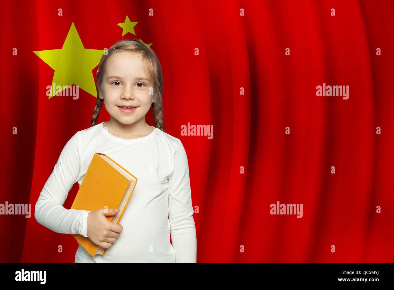 Impara il concetto di lingua cinese. Adorabile bambina con libro di testo contro bandiera di sfondo Cina. Foto Stock