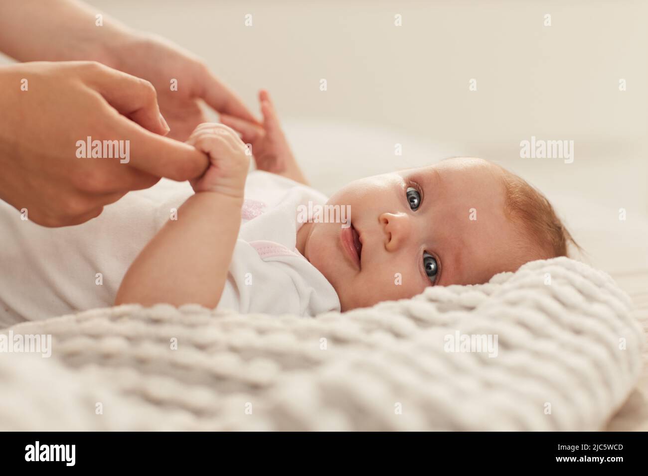 Bambina piccola con i grandi occhi grigi belli che stringono le dita di sua madre e guardando la macchina fotografica Foto Stock