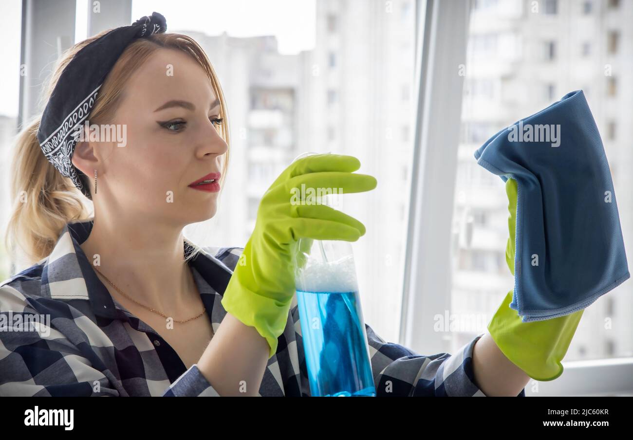 Concetto di housework e di housekeeping - donna in guanti lava finestra con straccio e detergente a casa Foto Stock