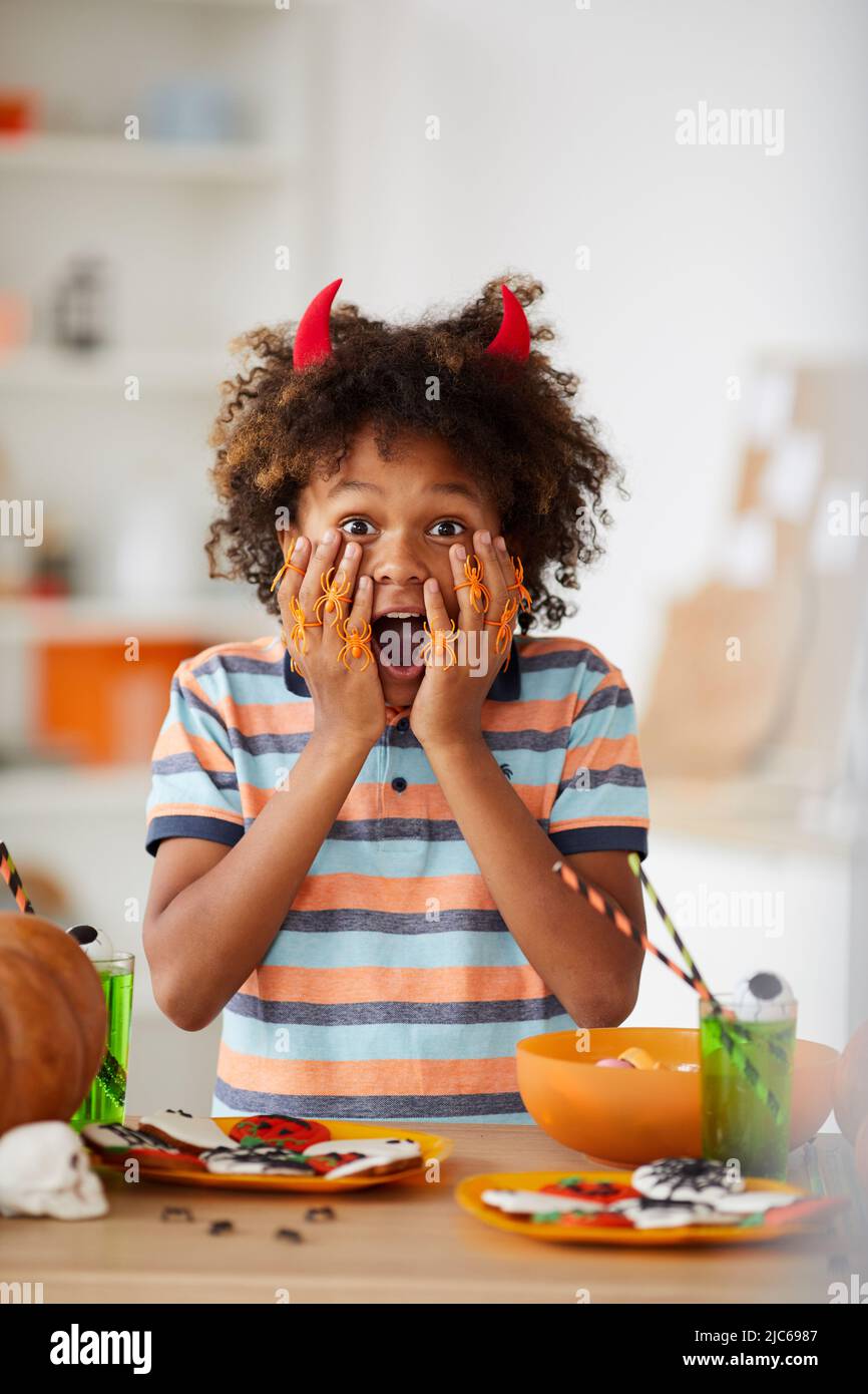 Ritratto di emotivo sorpreso Afro-americano ragazzo in corna rosse eccitato circa Halloween mantenere bocca aperta in cucina Foto Stock