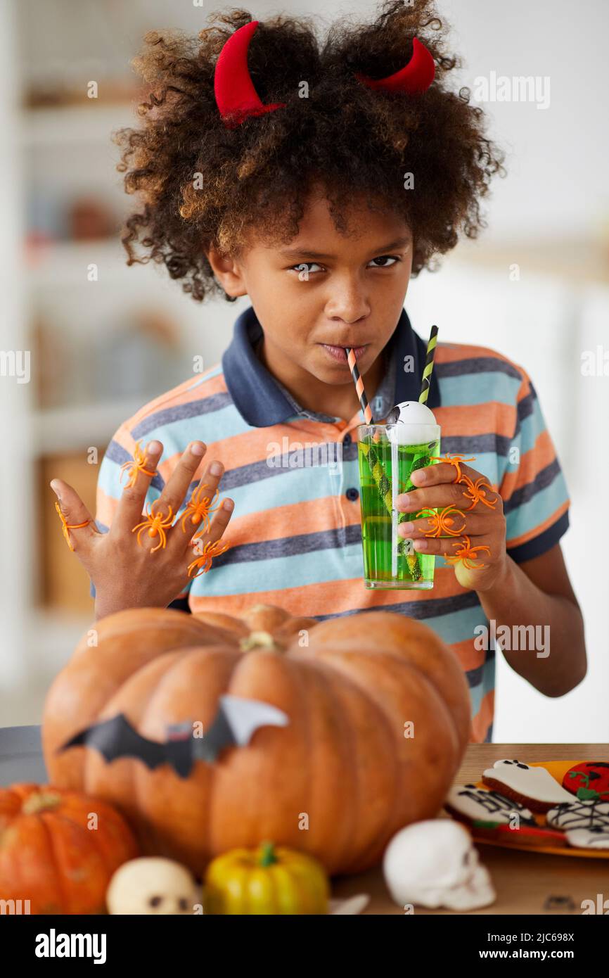 Contenuto Slug Afro-American ragazzo in corna rosse mostrando mano con anelli ragno di gomma sulle dita e bere limonata verde a Halloween Foto Stock
