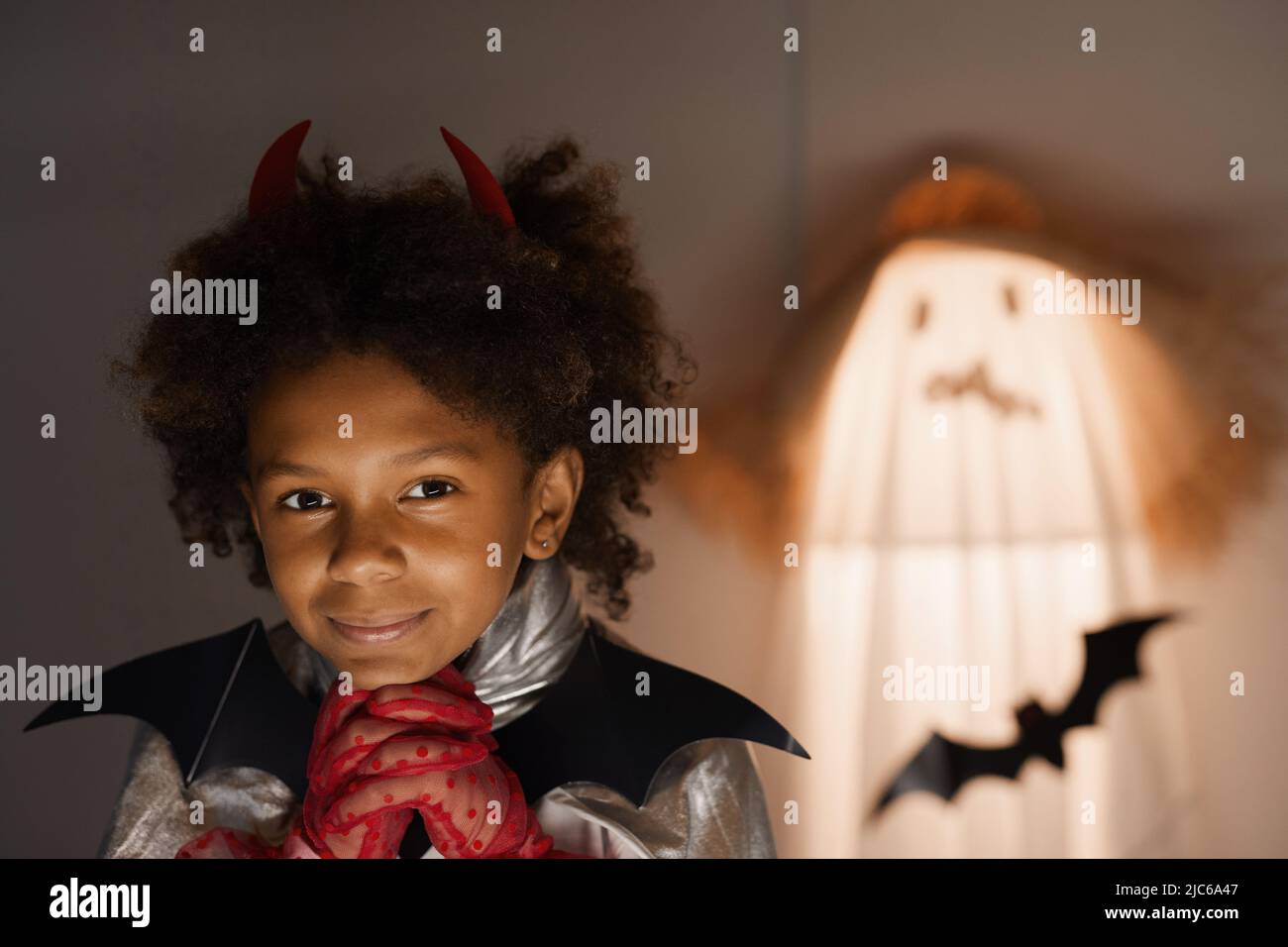 Ritratto di ragazzo afro-americano da sogno in abito Halloween testa appoggiata sulle mani in guanti rossi in camera scura Foto Stock