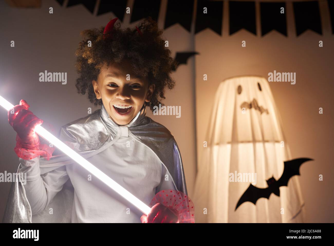 Ritratto di positivo estatico afroamericano ragazzo con bocca aperta tenendo incandescente bastone luce, Halloween partito concetto Foto Stock