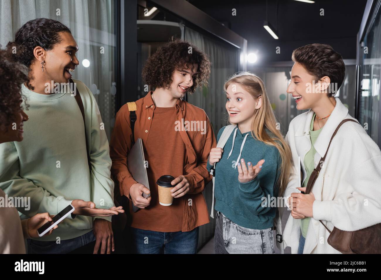 allegri studenti multiculturali che parlano e gesturano nel corridoio universitario Foto Stock