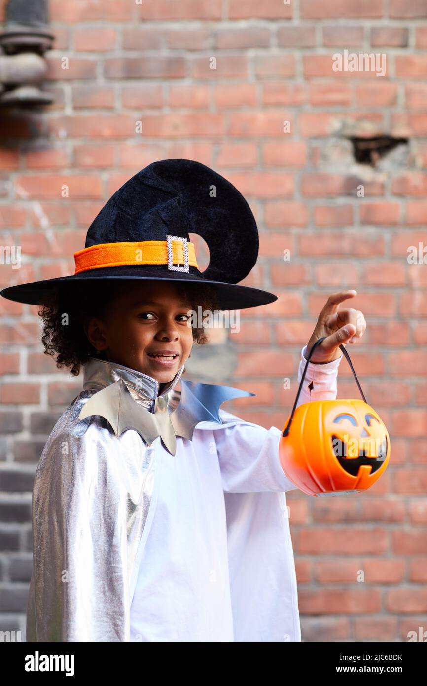 Ritratto di allegro ragazzo afroamericano carino in maghi cappello che tiene Halloween contenitore per trucco o trattare Foto Stock