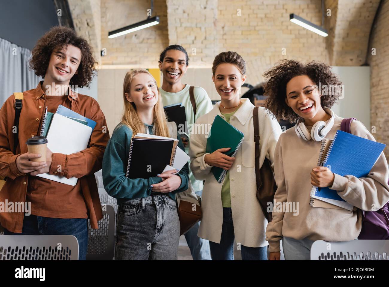 felice studenti multietnici con copybook e gadget che guardano la macchina fotografica in auditorium universitario Foto Stock
