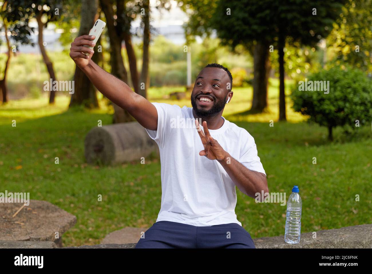 Giovane uomo adulto che riposa nel parco dopo aver fatto jogging e preso un selfie. Stile di vita sano. Foto Stock