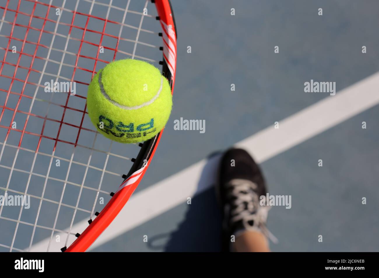 Staffa da tennis Red Wilson con palla da tennis Head Pro e scarpe nere  sotto di loro. Immagine a colori closeup dalla vista ad angolo alto.  Fotografato nella soleggiata Dubai Foto stock -