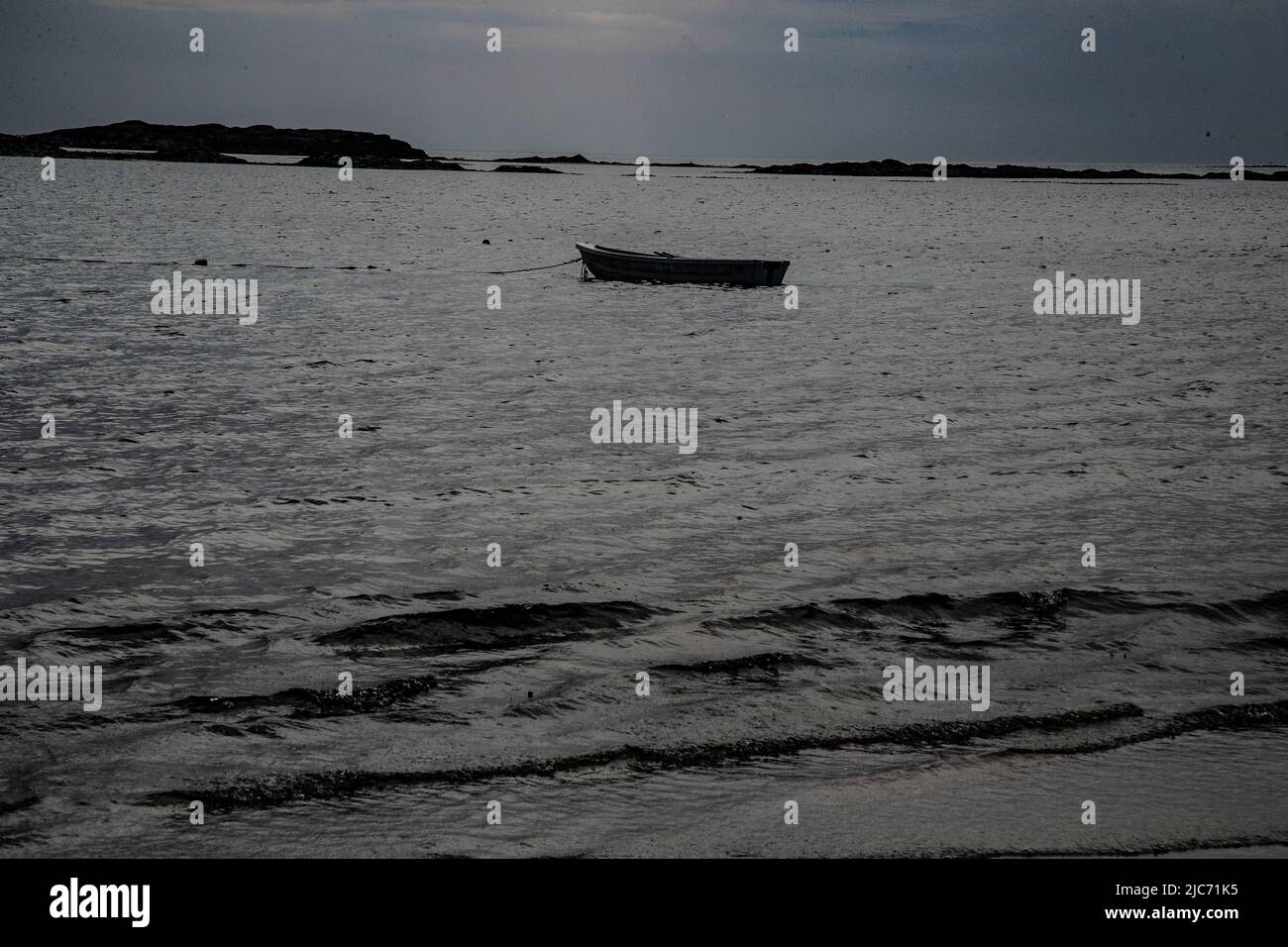 Piccolo dinghy all'ancora al largo della riva di una spiaggia in Uist del nord, Ebridi esterne come la sera cade con isole adiacenti visibili sullo sfondo Foto Stock