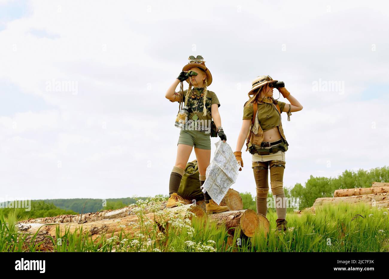Due ragazze giovani sono viste come esploratori. Osservano la campagna all'aperto. Sono vestiti con cappelli safari, binocoli e abiti da safari kaki. Foto Stock